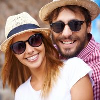 Happy girl and her boyfriend in hats and sunglasses looking at camera